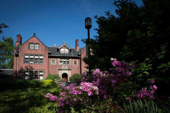 Lush spring greenery and pink flowers are in the foreground, with a red brick academic building in the background